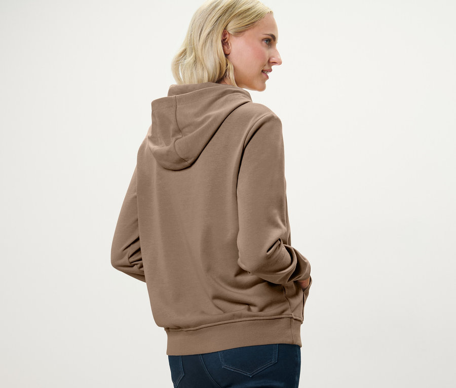 Une femme blonde porte un sweat à capuche beige.