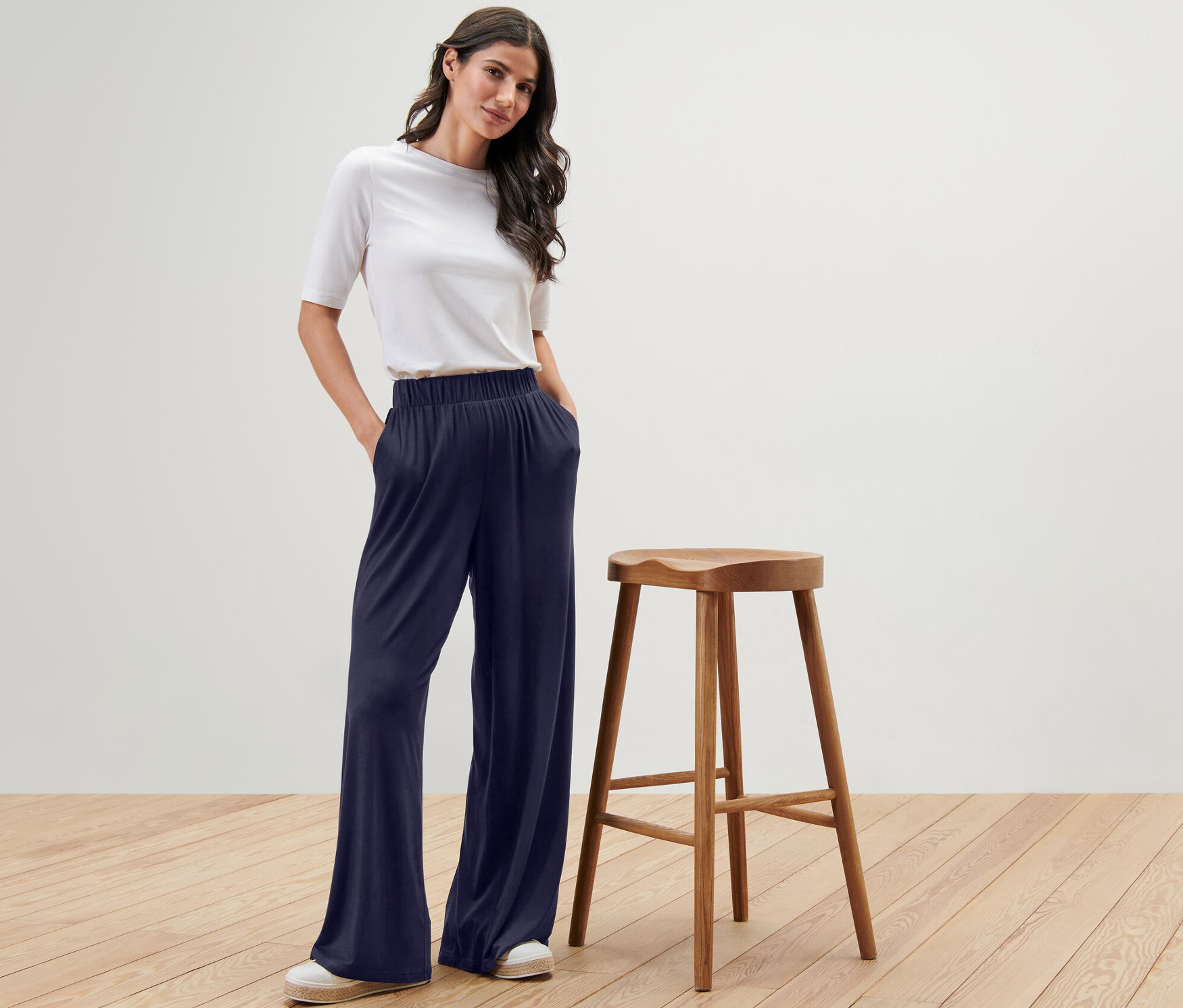 Une femme pose en pantalon palazzo bleu foncé à côté d'un tabouret en bois.