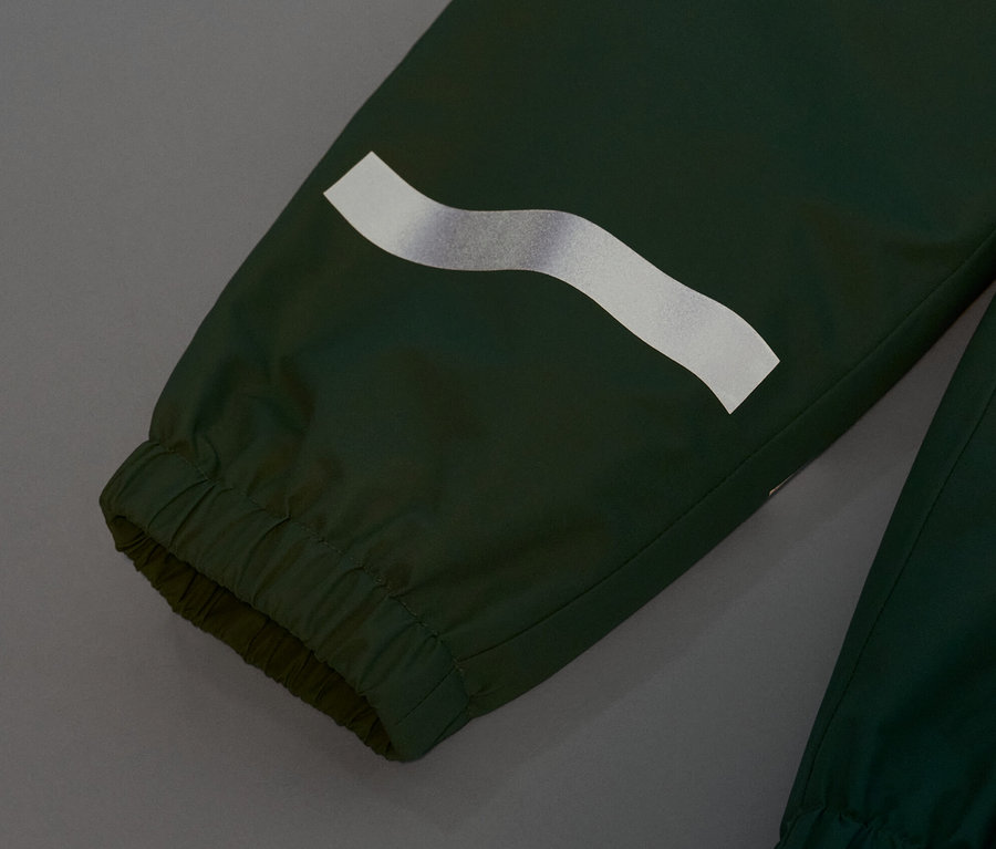 Gros plan sur un pantalon de pluie pour enfant vert gazon avec une bande réfléchissante.