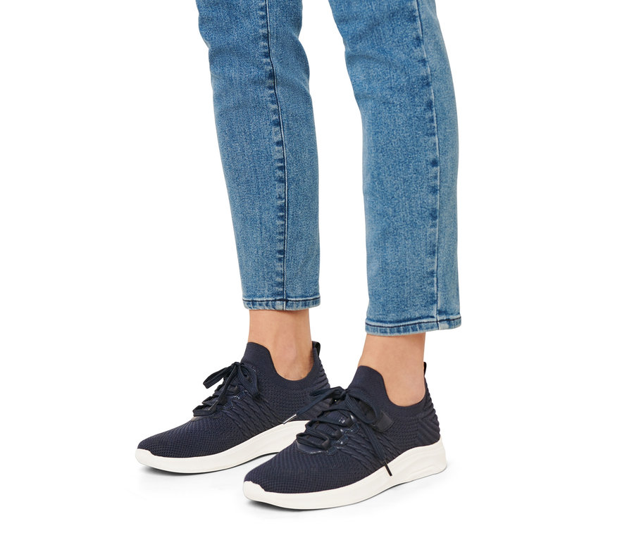 Jambes d'une personne portant un jean et des tennis slip-on bleues à semelles blanches.