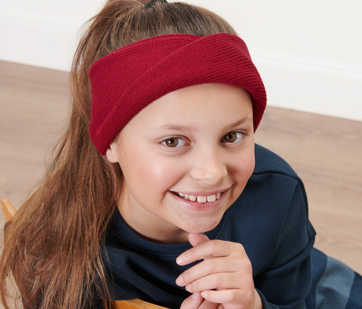 Une fille assise sur une chaise portant un bandeau en tricot pour enfant.
