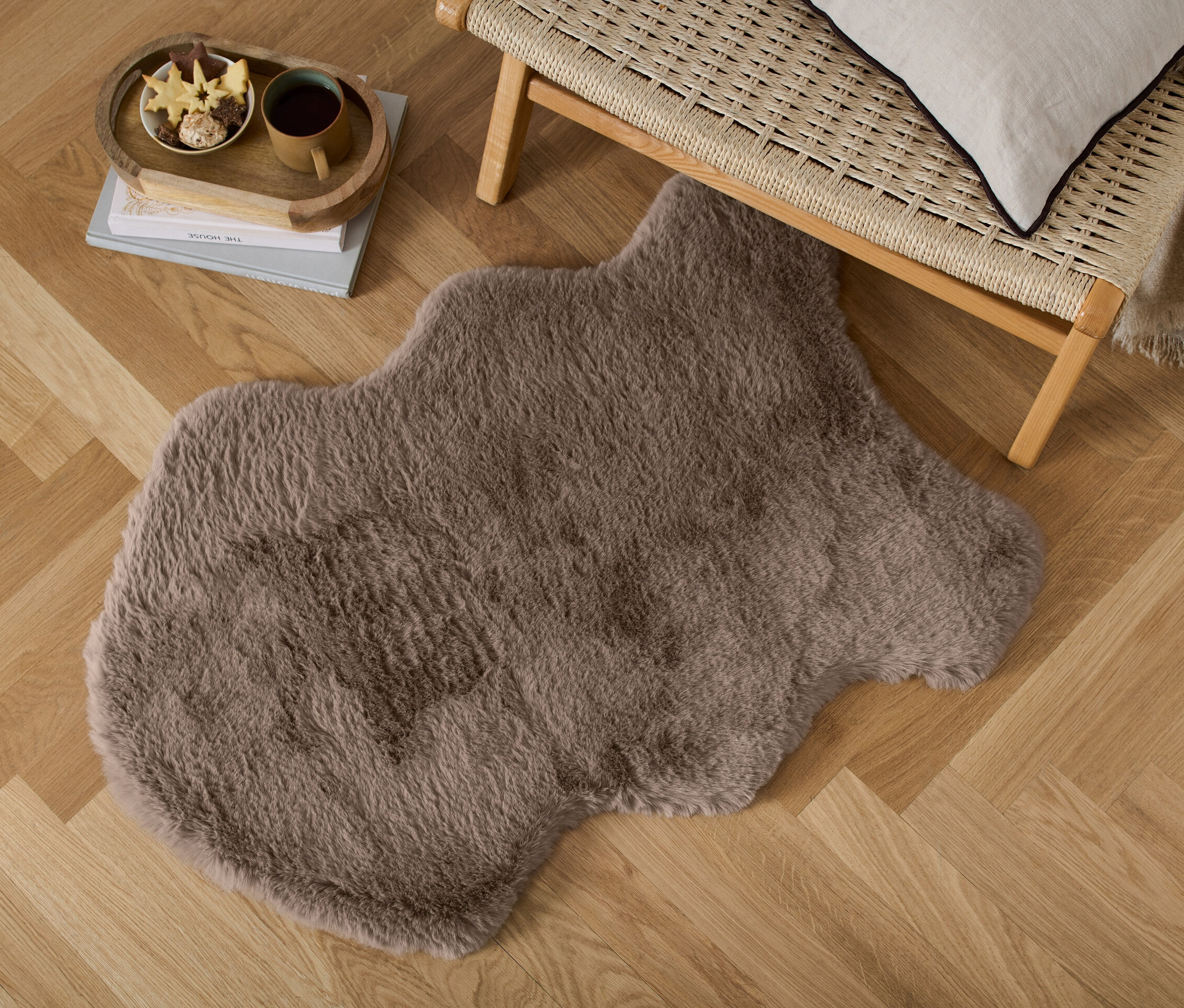 Une fausse fourrure décorative est posée sur un parquet à chevrons, à côté d'une banquette en osier.