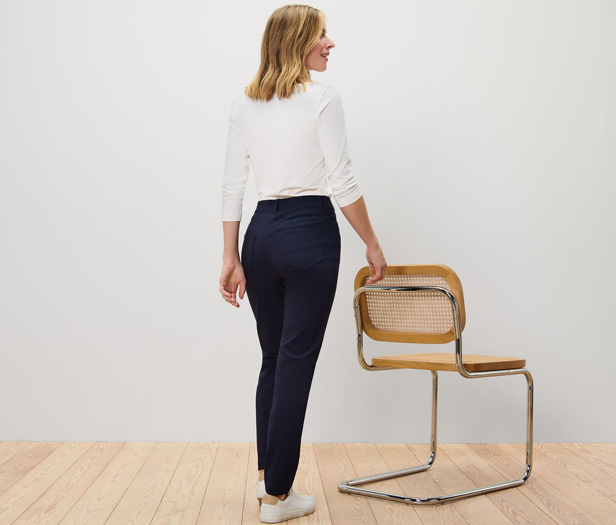 Une femme, vue de dos, tient une chaise. Elle porte un pantalon en bengaline bleu foncé.