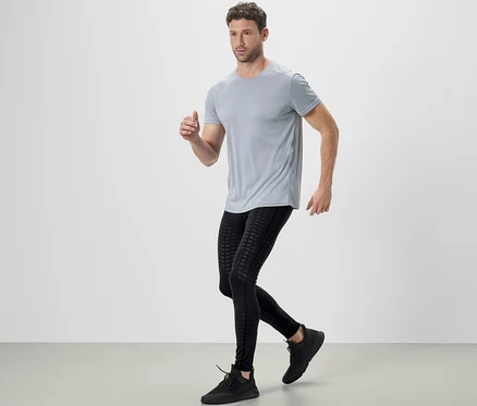 Un homme court, vêtu d'un t-shirt gris et d'un legging de sport noir.