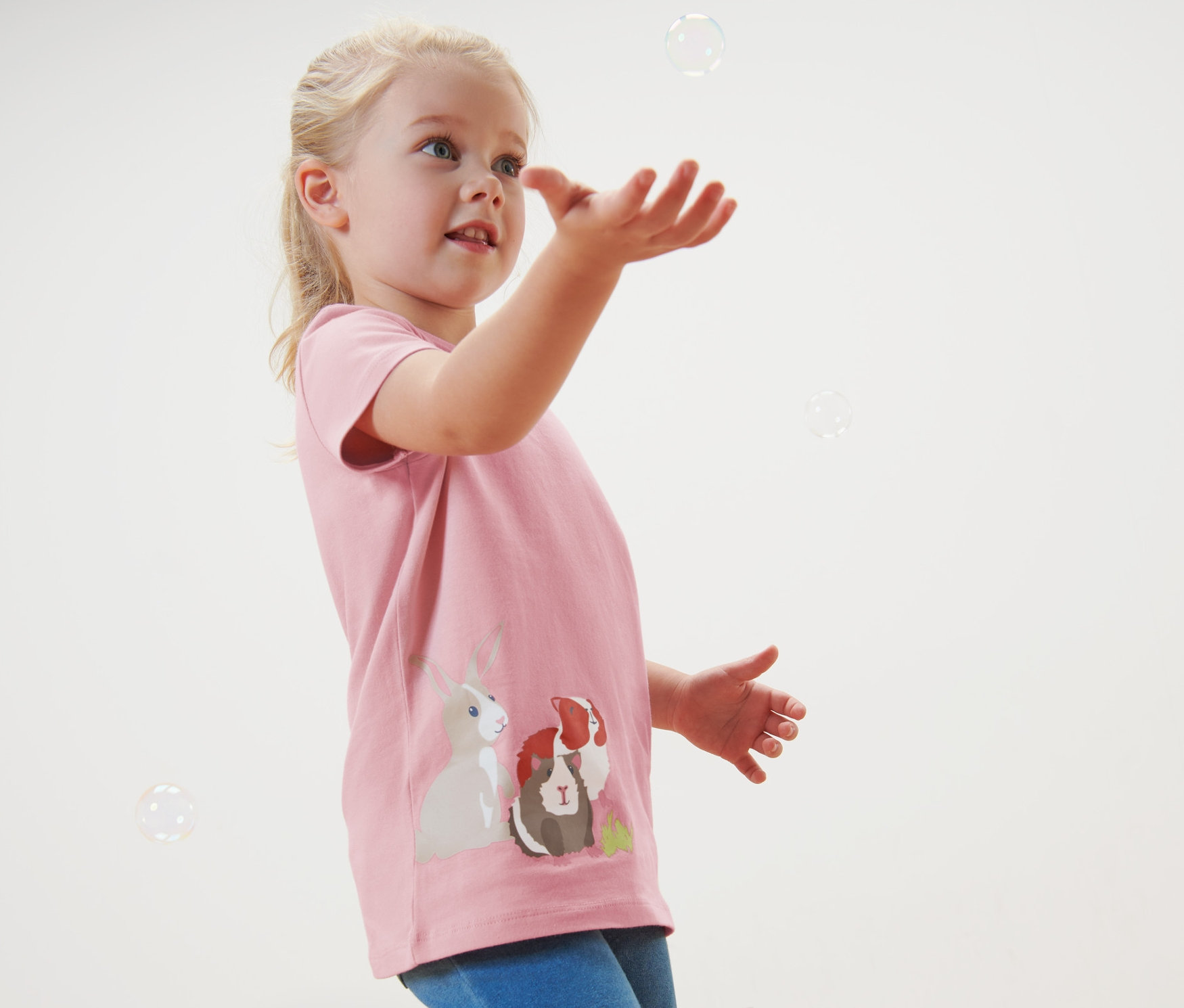 Une fillette attrape des bulles de savon. Elle porte un t-shirt rose avec des motifs d'animaux. 2 t-shirts pour tout-petit.