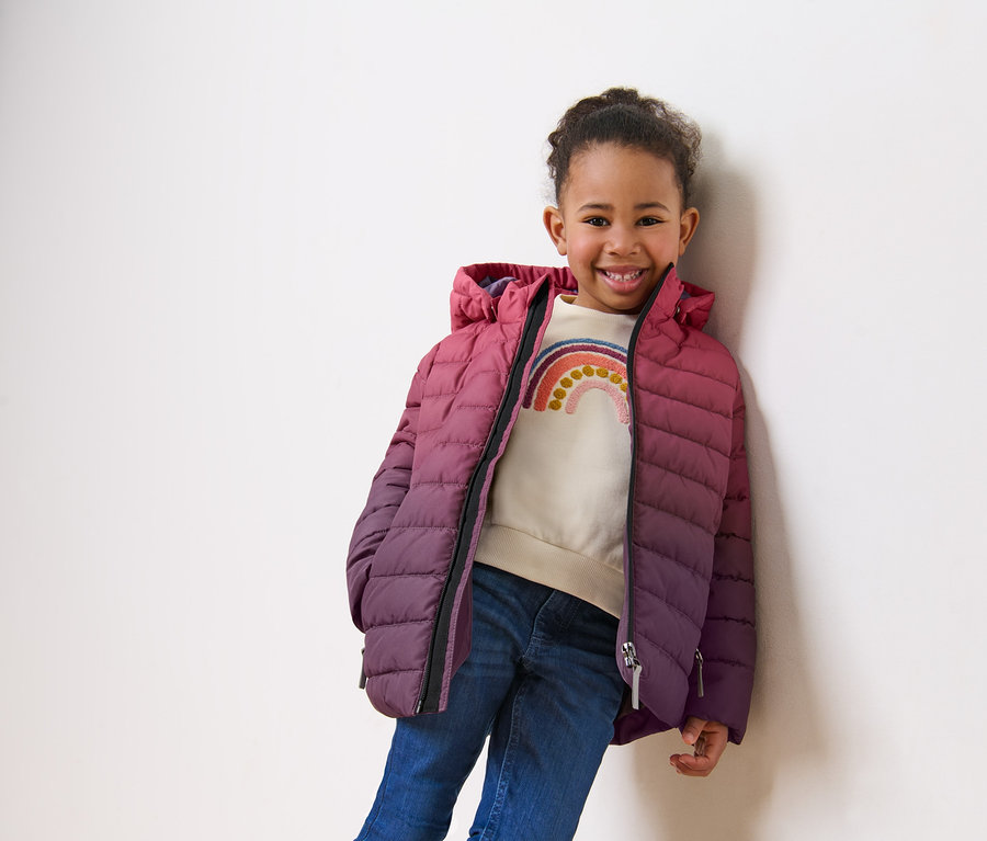 Fillette souriante posant en veste matelassée pour enfant avec un dégradé de couleurs.