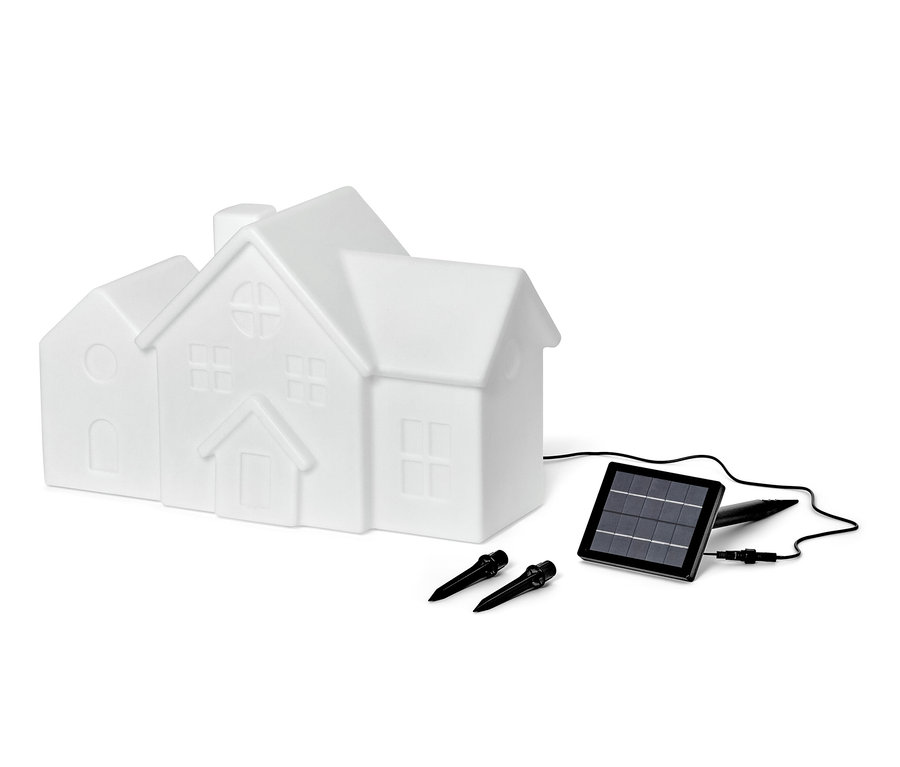 Une lampe solaire d'extérieur blanche en forme de maison, un panneau solaire et deux piquets de fixation sont présentés sur un fond blanc.