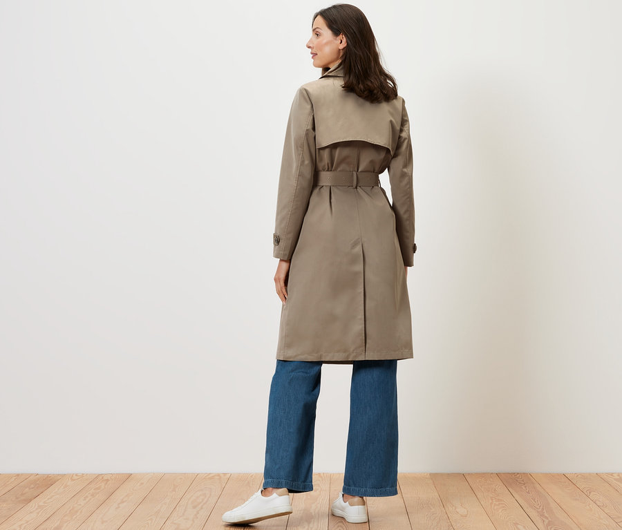 Femme debout, vue de dos, portant un trench-coat beige.