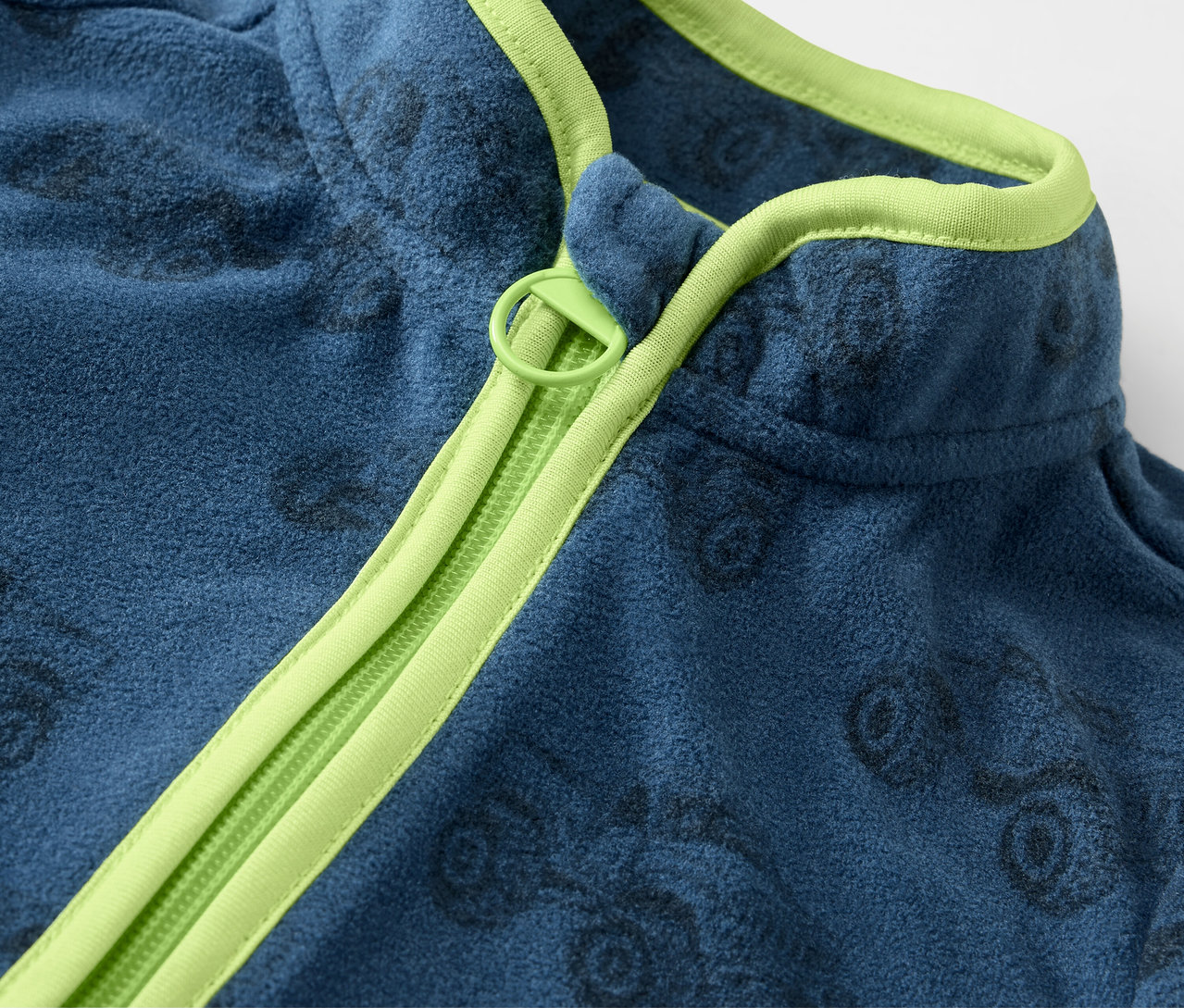 Gros plan sur une veste polaire bleue pour enfants avec des camions et une fermeture éclair vert clair.