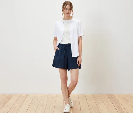 Une femme pose en short en mousseline, t-shirt et chemise.