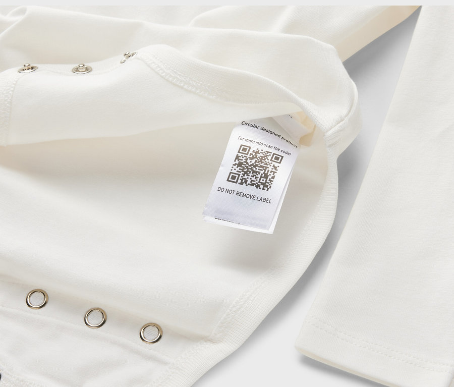 Gros plan sur un body évolutif blanc à manches longues pour bébé, avec une étiquette comportant un QR code.