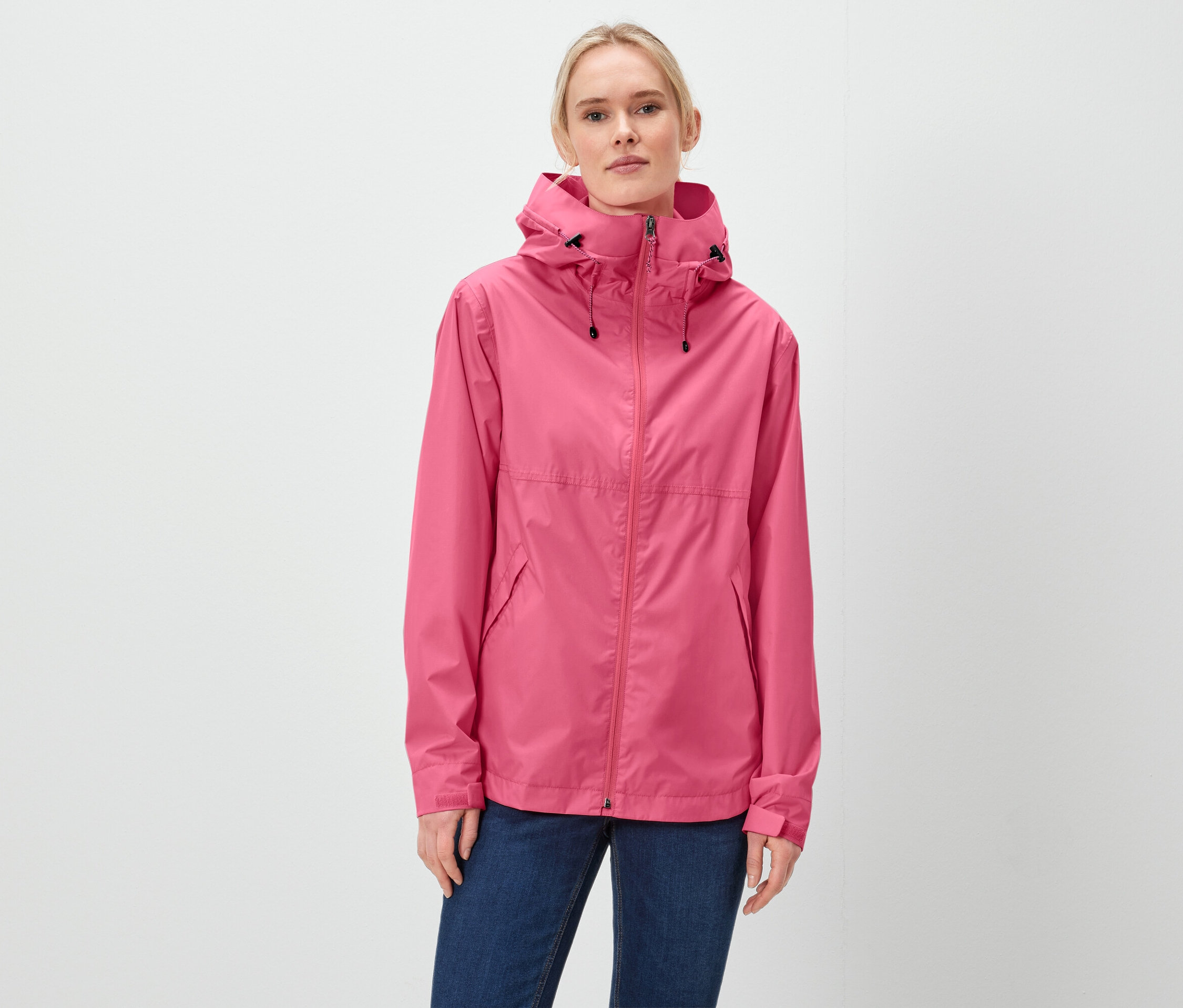 Une femme porte une veste rose à capuche et un jean bleu.