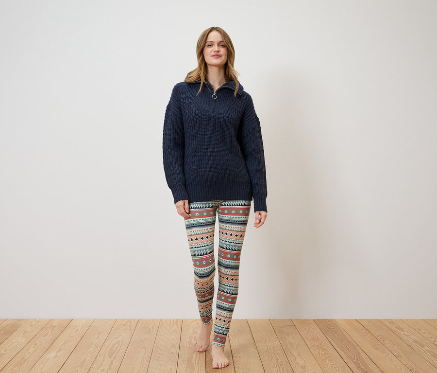 Une femme debout portant un pull bleu marine et un legging à motifs.