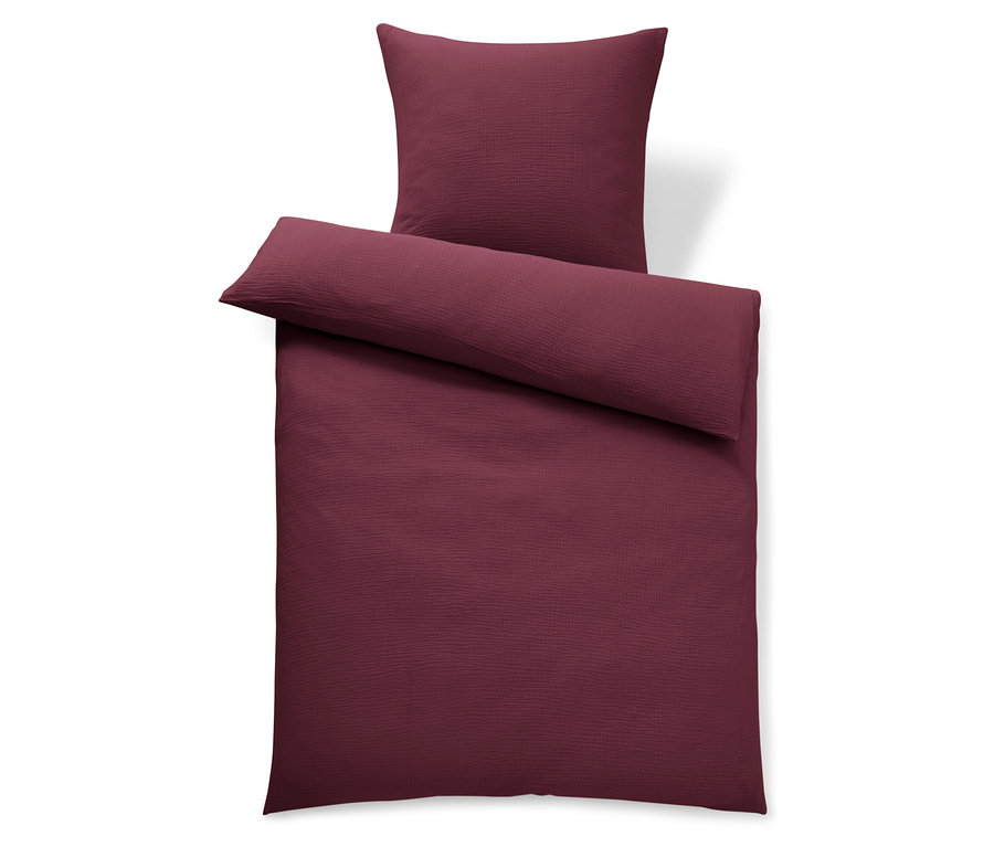Linge de lit bordeaux et oreiller sur fond blanc.