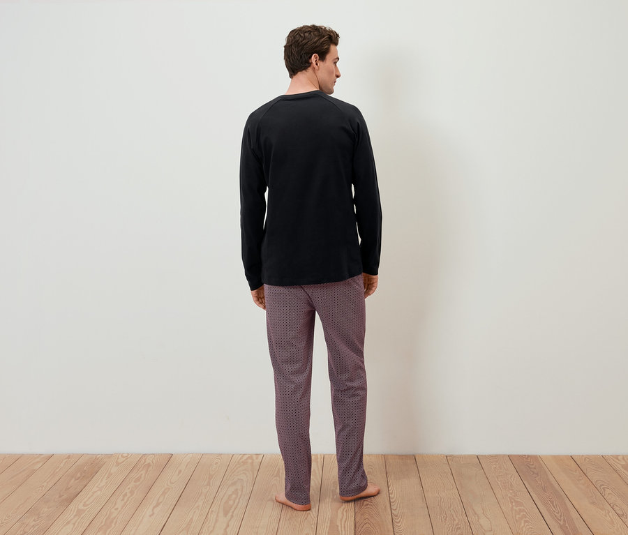 Un homme, dos à la caméra, porte un t-shirt noir à manches longues et un pantalon à motifs.