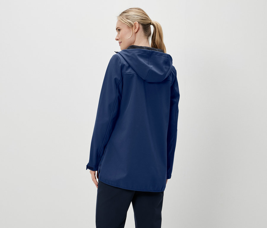 Vue arrière d'une femme aux cheveux blonds attachés en queue de cheval, portant une veste bleu foncé à capuche et un pantalon foncé.