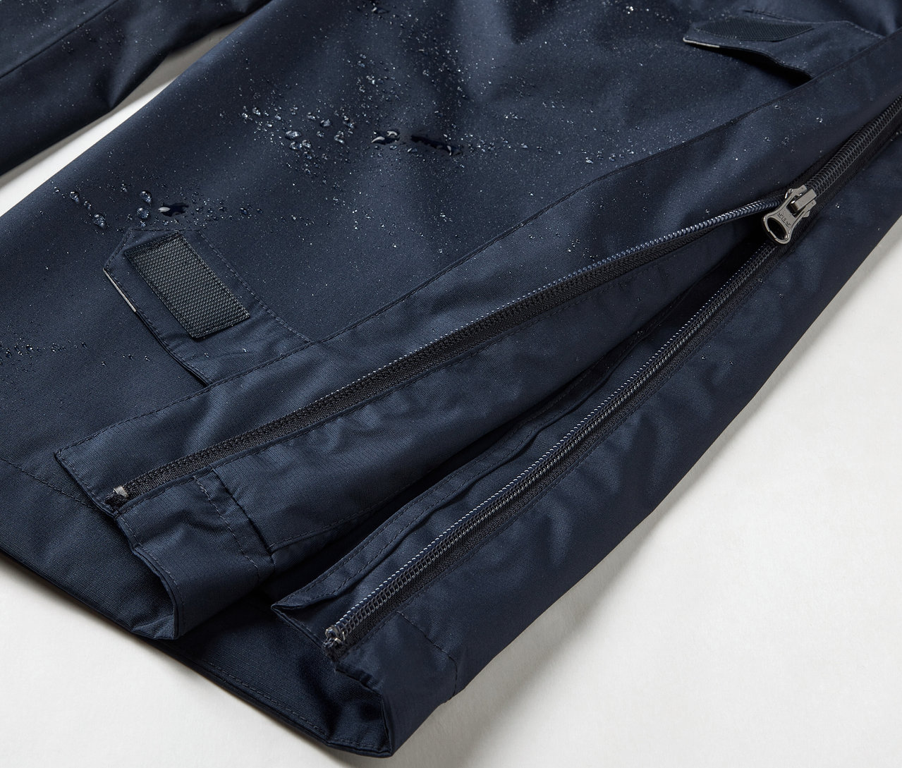 Gros plan sur un pantalon de pluie high-tech bleu marine avec fermeture éclair intégrale.
