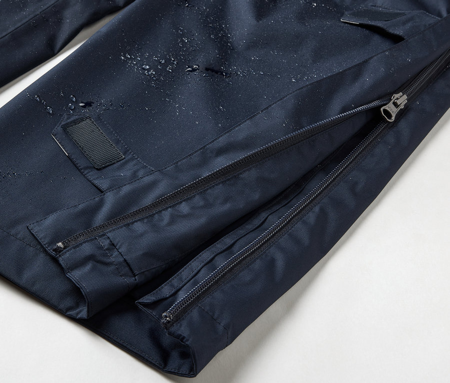 Gros plan sur un pantalon de pluie high-tech bleu marine avec fermeture éclair intégrale.