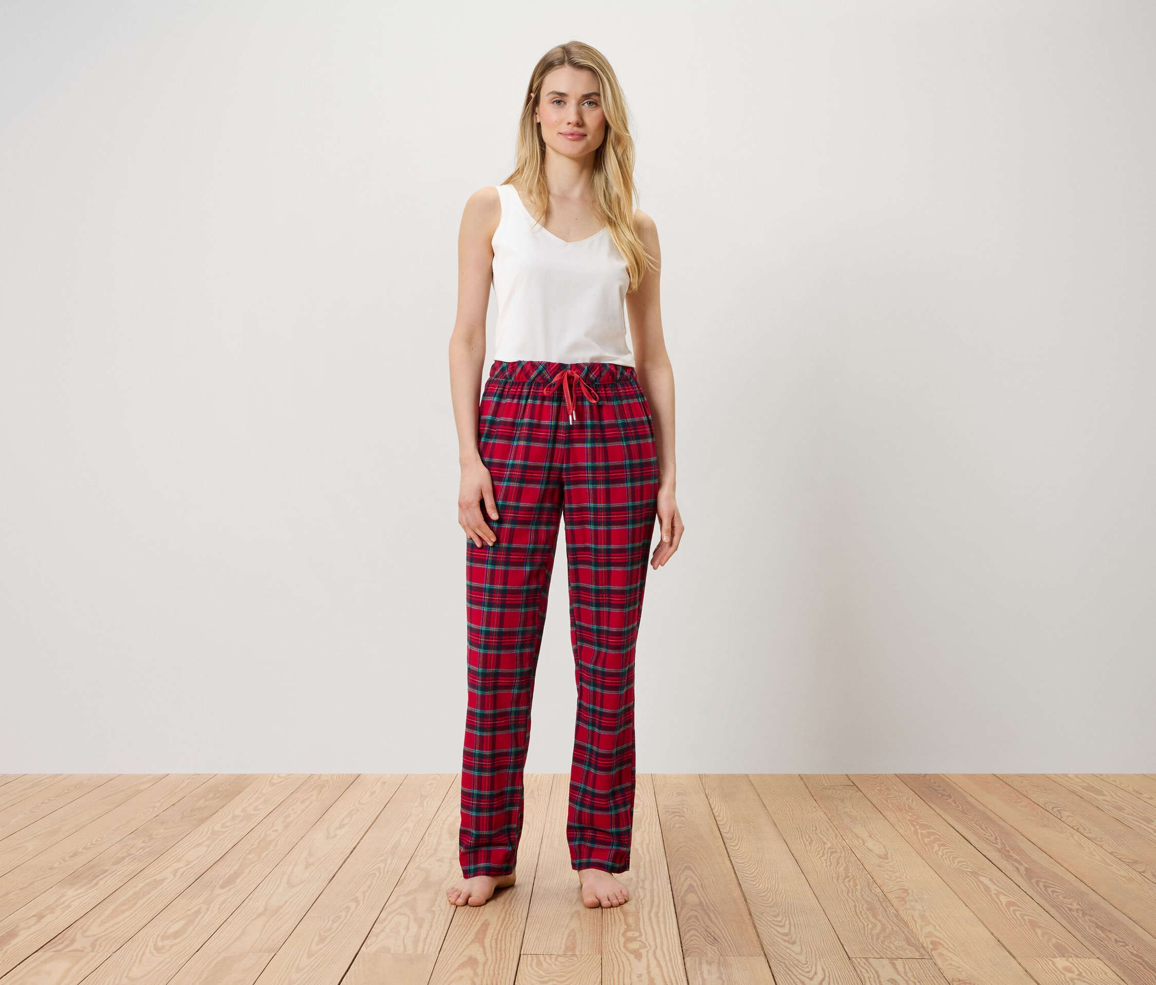 Une femme debout portant un haut blanc et un pantalon à carreaux rouge.