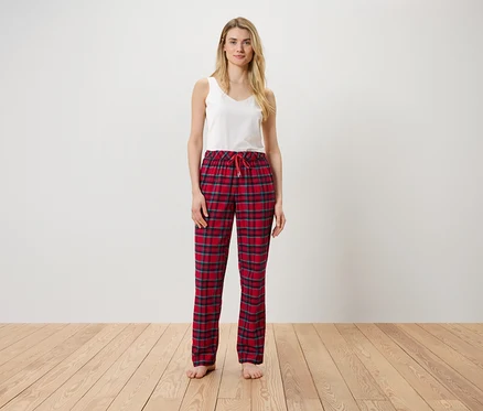 Une femme debout portant un haut blanc et un pantalon à carreaux rouge.