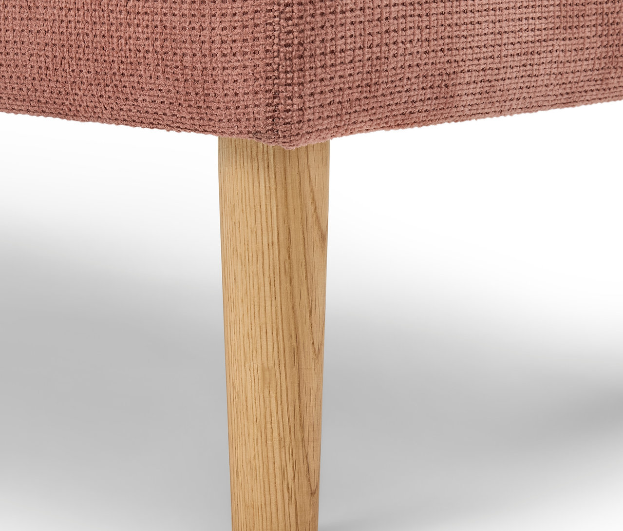 Détail d'un meuble rembourré rose avec un pied en bois.