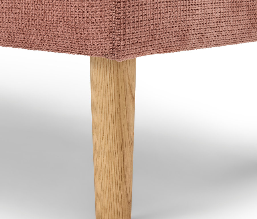 Détail d'un meuble rembourré rose avec un pied en bois.