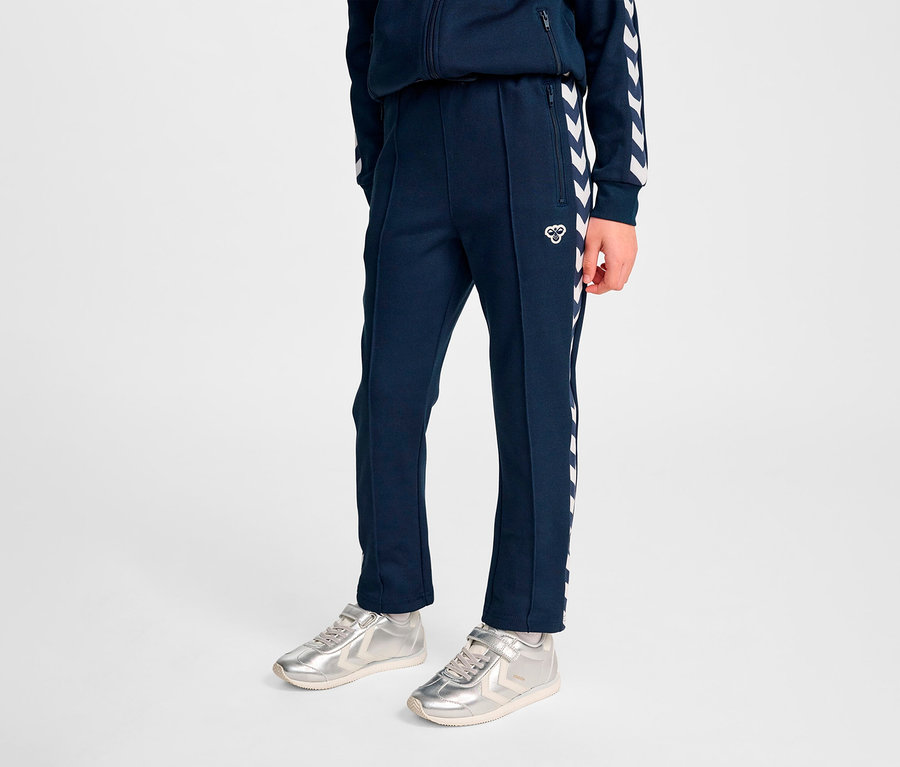 Personne debout portant un pantalon Regular Poly HUMMEL HMLJR Archive bleu marine et des baskets argentées.