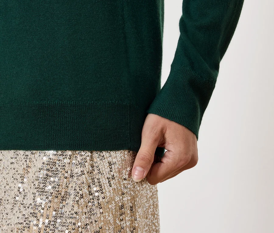 Détail d'une tenue féminine : pull vert et jupe dorée à paillettes.