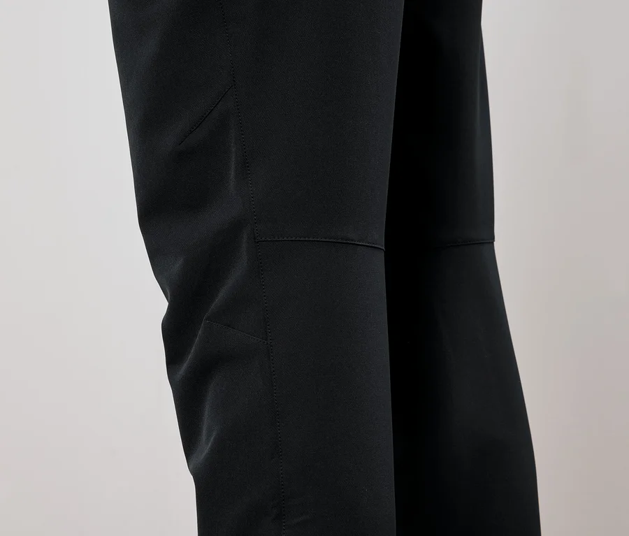 Détail d'un pantalon noir avec des patchs aux genoux.