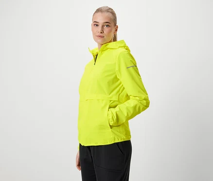 Blonde portant une veste à capuche jaune néon et un pantalon noir, posant de profil.