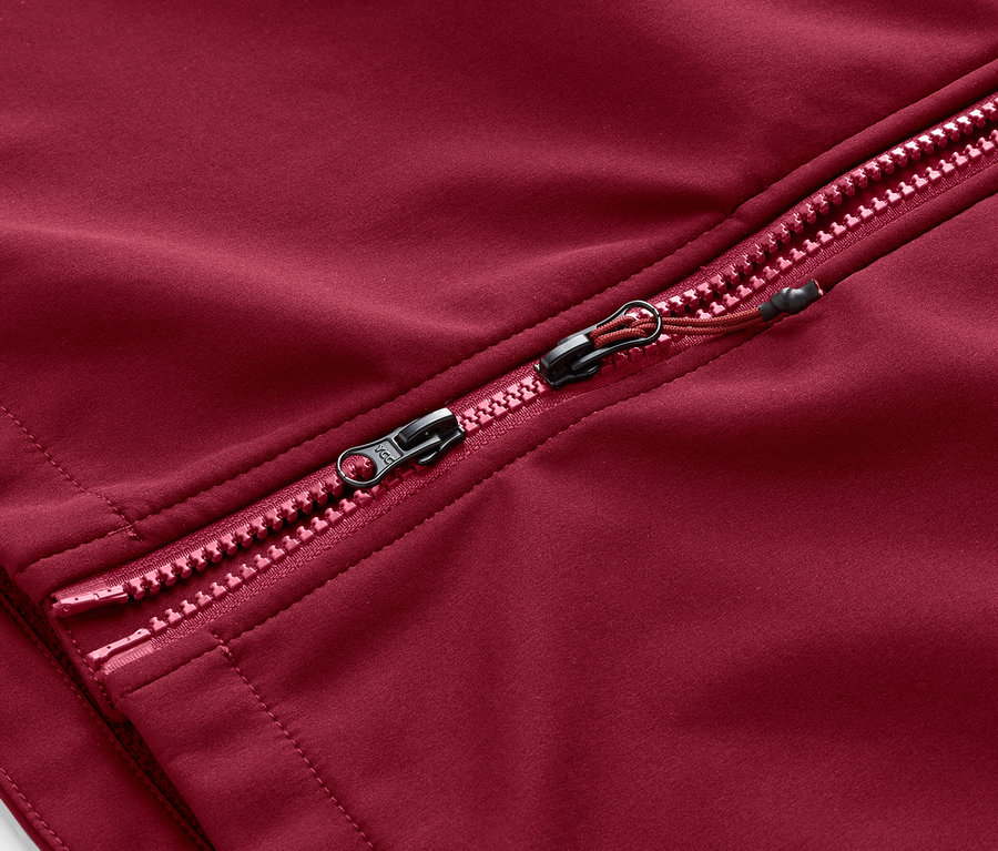 Gros plan sur la fermeture éclair d'un manteau en softshell rouge foncé.