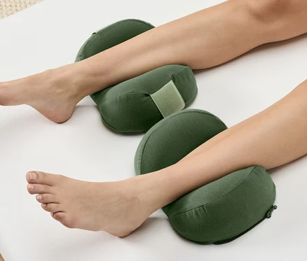 Les jambes d'une femme reposent sur deux coussins verts sur fond blanc.