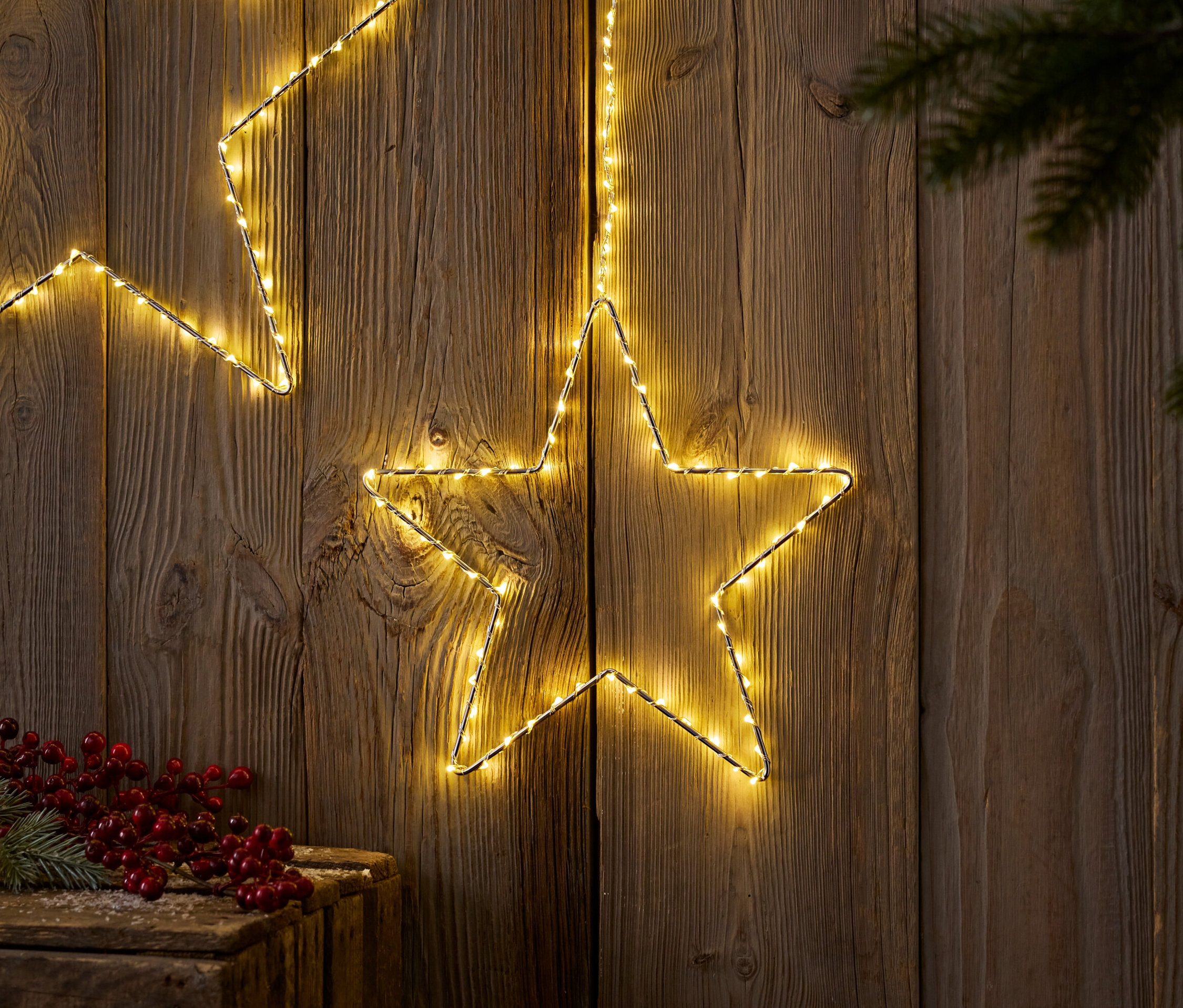 Deux étoiles lumineuses sur fond de bois avec branche de sapin et baies rouges.