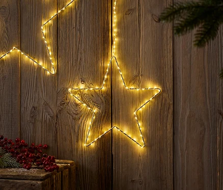 Deux étoiles lumineuses sur fond de bois avec branche de sapin et baies rouges.