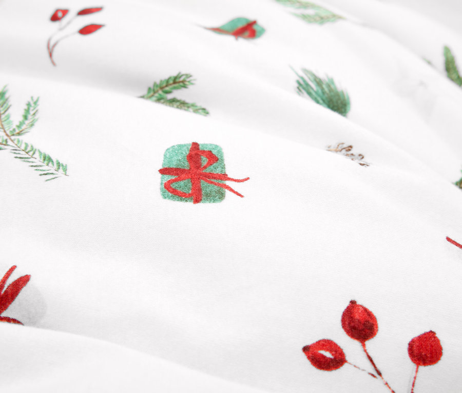 Gros plan sur un tissu avec des motifs de Noël, des branches vertes et des baies rouges.