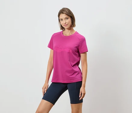 Une femme porte un t-shirt rose avec un motif de chaîne de montagnes et un short bleu marine sur un fond blanc.