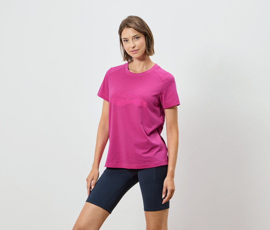 Une femme porte un t-shirt rose avec un motif de chaîne de montagnes et un short bleu marine sur un fond blanc.