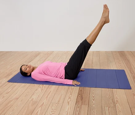 Femme allongée sur un tapis de yoga bleu, les jambes levées.