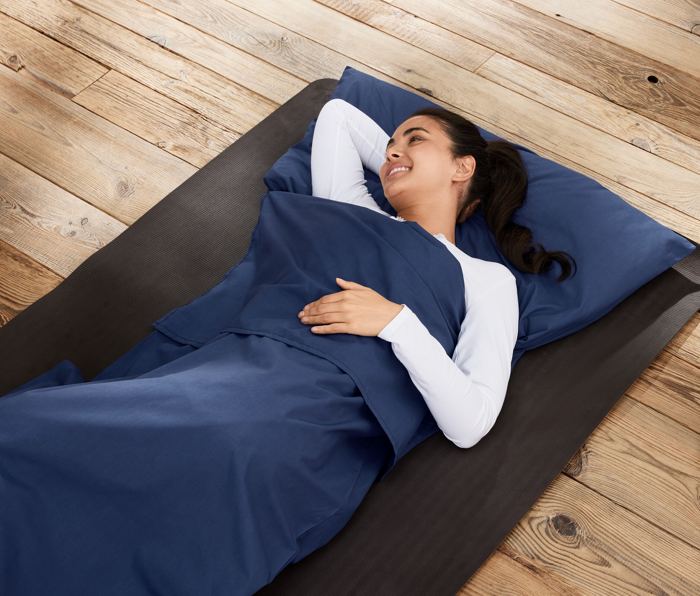 Une femme allongée dans une doublure pour sac de couchage sur un tapis sur un plancher en bois.
