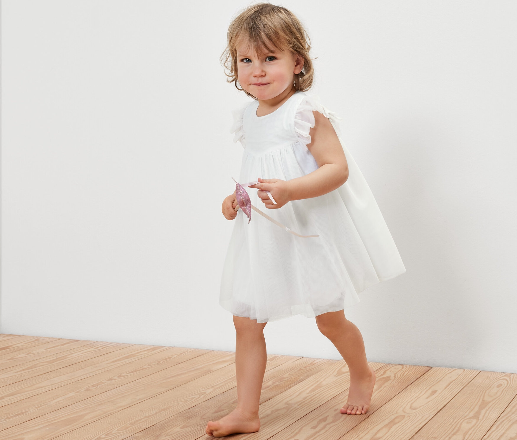 Petite fille marchant sur un plancher en bois et portant une robe en tulle pour bébé.