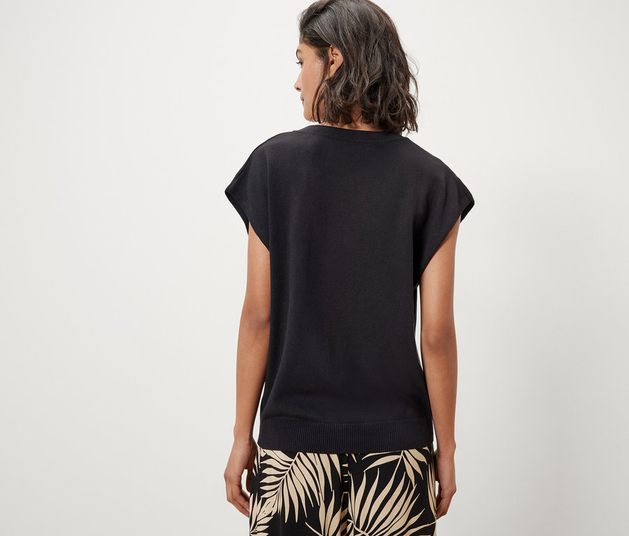 Vue arrière d'une femme portant un pull-over noir en maille fine à manches courtes et une jupe à imprimé de palmiers.