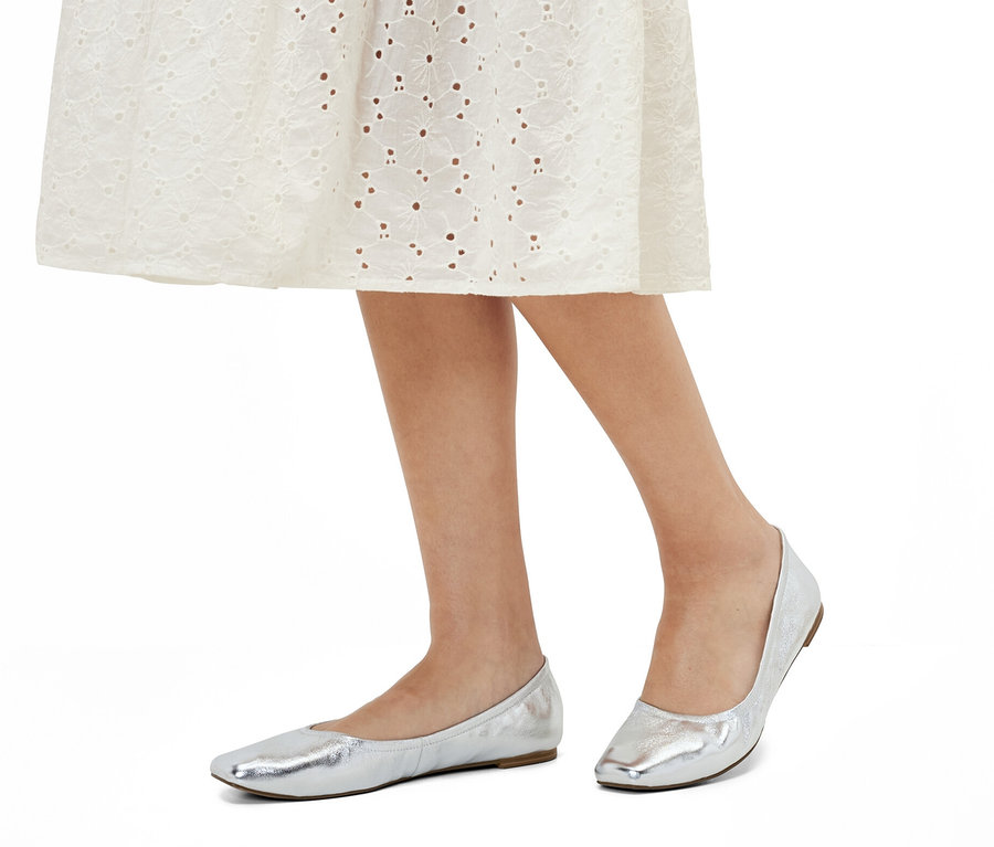 Jambes d"une femme en robe blanche et ballerines en cuir.