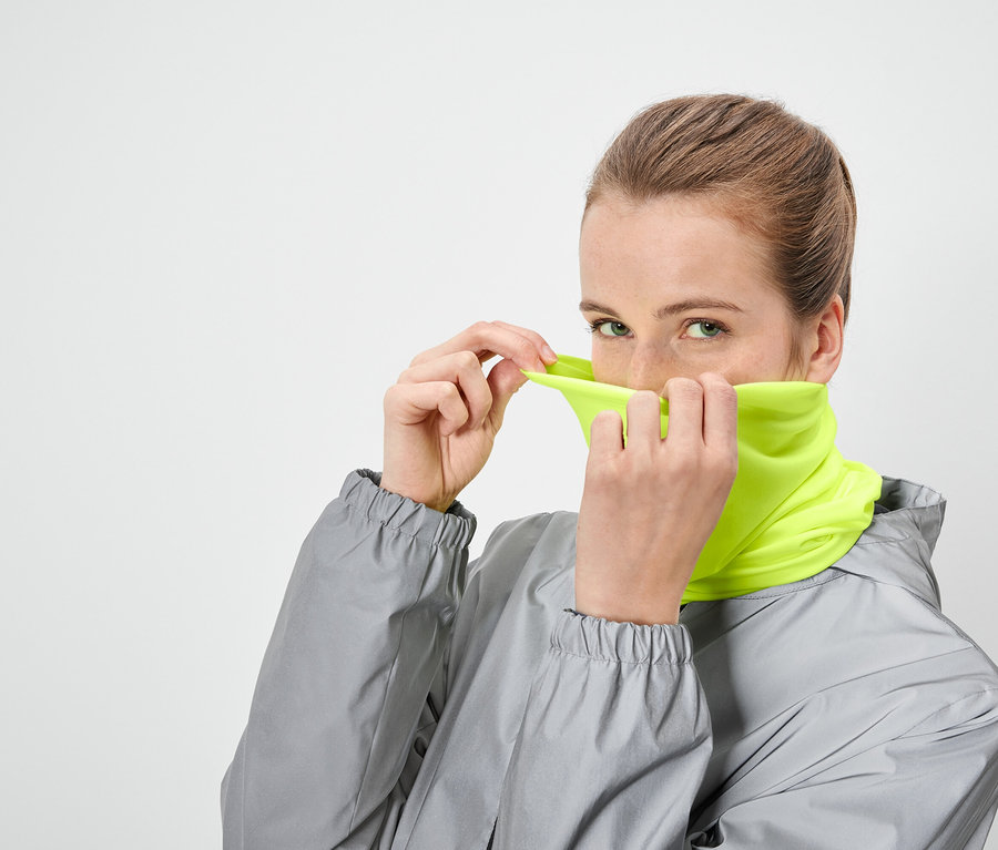 Une femme remonte un cache-cou jaune néon sur son visage et porte une veste grise.