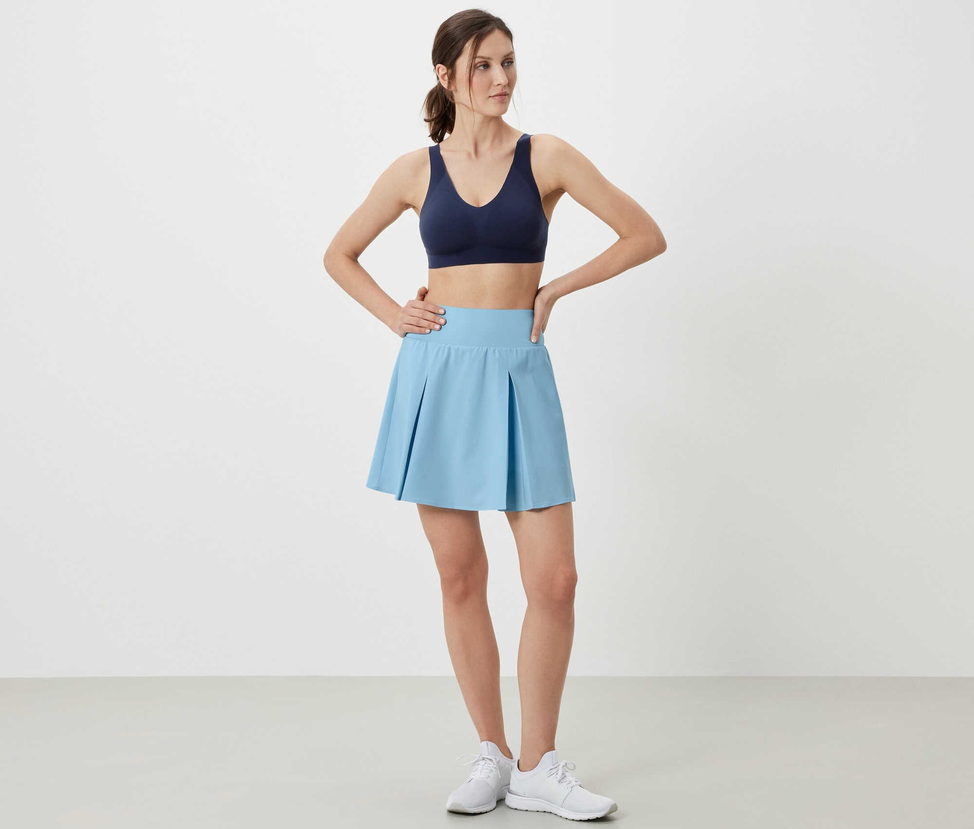 Femme posant en jupe de sport bleu clair et soutien-gorge de sport.