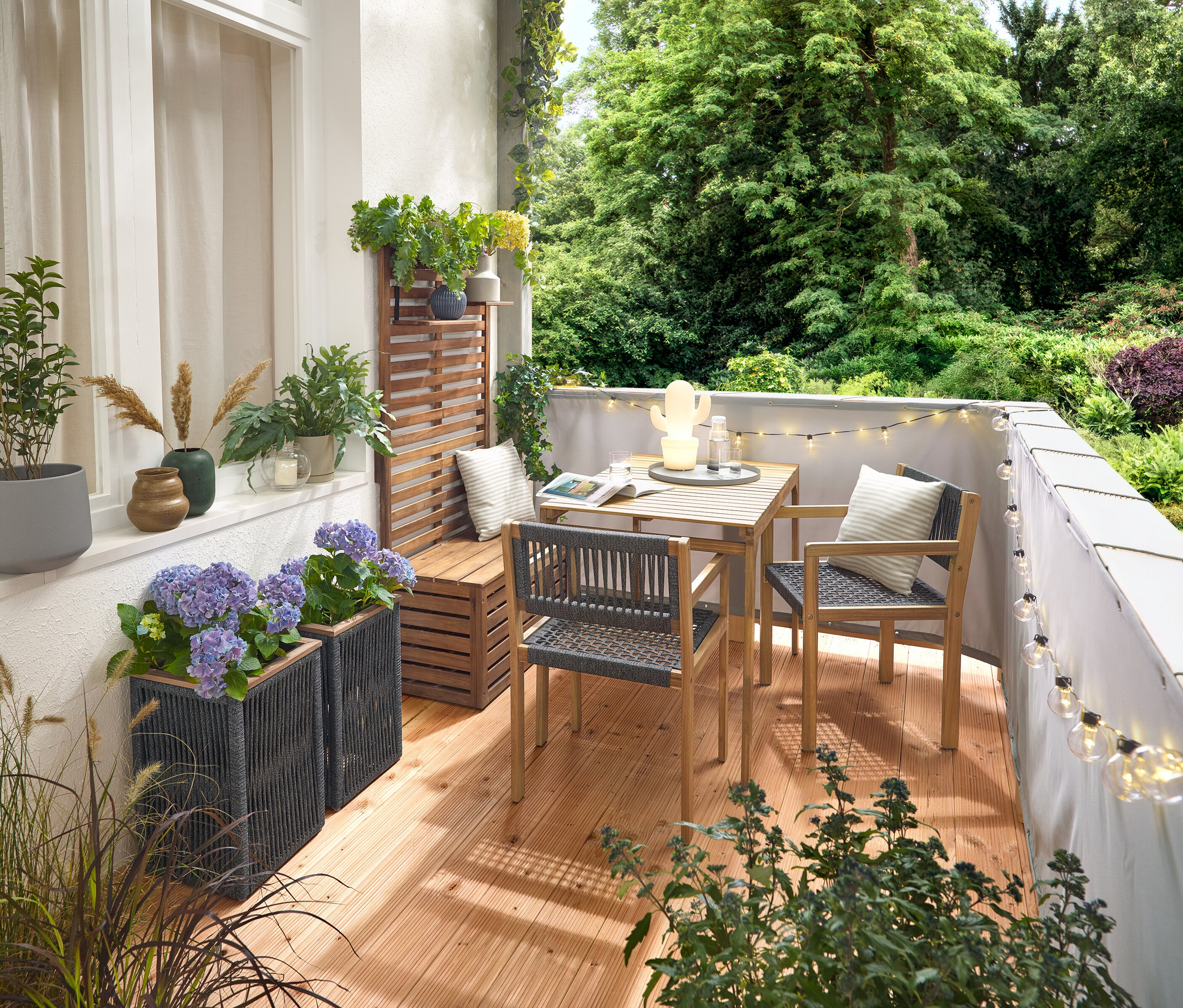 Aménagement d'un balcon avec un ensemble de balcon avec tressage textile, un brise-vue et brise-vent pour balcon gris, une guirlande lumineuse LED d'extérieur avec adaptateur secteur, un pot de fleurs avec tressage textile, une lampe de table LED d'extérieur à batterie en forme de cactus et 2 coussins d'extérieur à l'aspect lin.