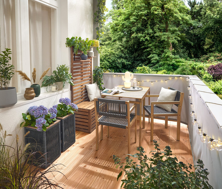 Aménagement d'un balcon avec un ensemble de balcon avec tressage textile, un brise-vue et brise-vent pour balcon gris, une guirlande lumineuse LED d'extérieur avec adaptateur secteur, un pot de fleurs avec tressage textile, une lampe de table LED d'extérieur à batterie en forme de cactus et 2 coussins d'extérieur à l'aspect lin.