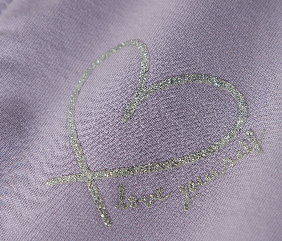 Gros plan d'un vêtement violet avec un motif de cœur scintillant et le texte "love yourself".
