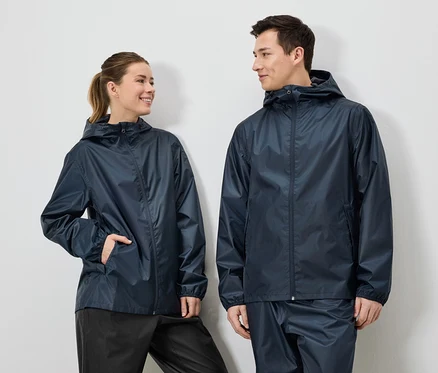 Une femme avec une queue de cheval et un homme portent des vestes de pluie et des pantalons de pluie bleu marine sur un fond blanc.