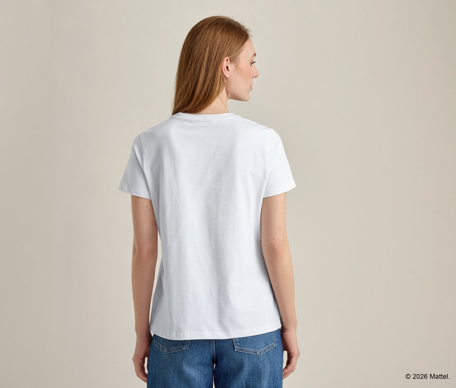 Vue de dos d'une femme aux longs cheveux roux portant un t-shirt blanc et un jean bleu.