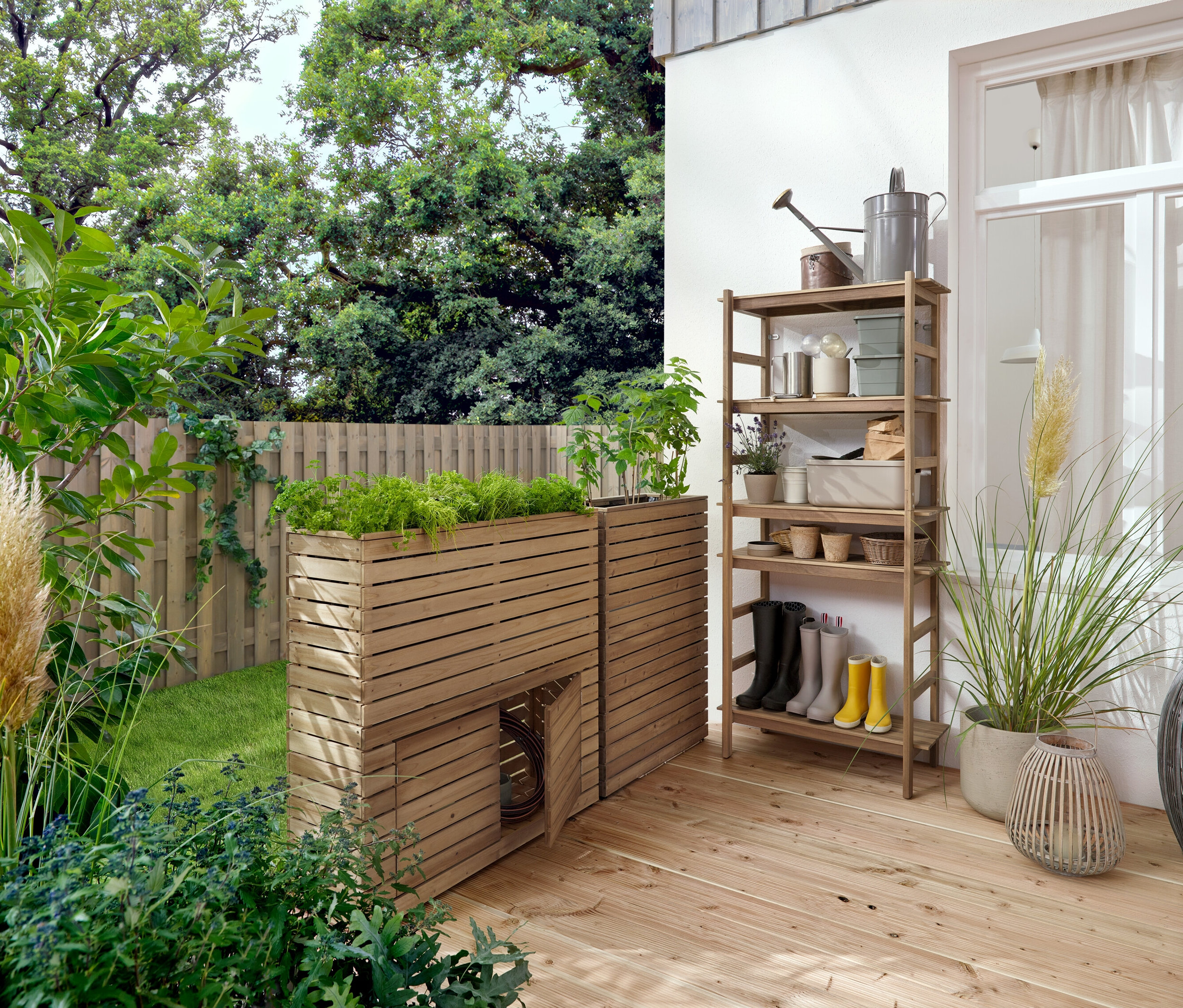 Sur une terrasse en bois se trouvent deux jardinières en bois et une étagère avec des accessoires de jardin.